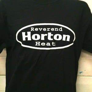 May include: Black t-shirt with a white oval logo that says "Reverend Horton Heat".