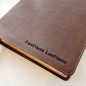 May include: Brown leather-bound journal with gold-colored edges and the name "FirstName LastName" embossed on the front cover.