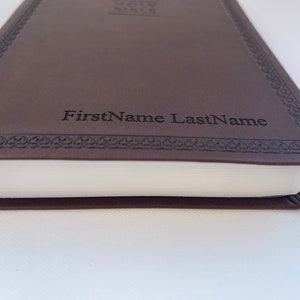 K&ouml;nnte beinhalten: Ein braunes, ledergebundenes Tagebuch mit einem dekorativen Rand und dem Namen "FirstName LastName" auf der Vorderseite gepr&auml;gt.