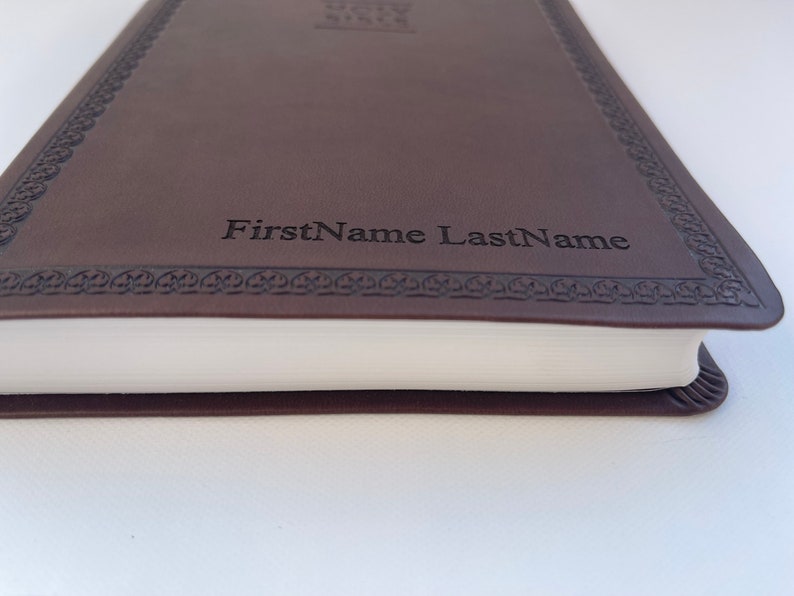 K&ouml;nnte beinhalten: Ein braunes, ledergebundenes Tagebuch mit einem dekorativen Rand und dem Namen "FirstName LastName" auf der Vorderseite gepr&auml;gt.