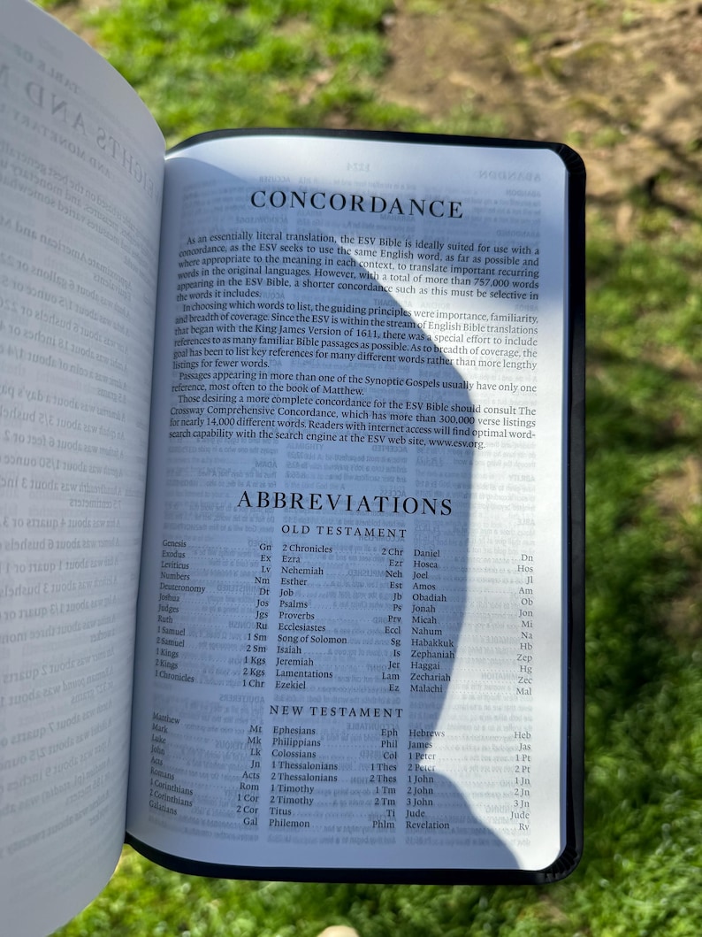 Pode incluir: B&iacute;blia aberta com as palavras "CONCORDANCE" e "ABBREVIATIONS". As p&aacute;ginas exibem listas de termos e refer&ecirc;ncias b&iacute;blicas. A B&iacute;blia tem uma capa preta e est&aacute; aberta na grama.