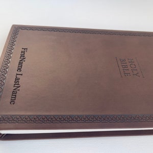 K&ouml;nnte beinhalten: Eine braune, ledergebundene Heilige Bibel mit einem dekorativen Rand und den Worten "HOLY BIBLE" auf dem vorderen Einband. Der Name "FirstName LastName" ist ebenfalls auf dem Einband gepr&auml;gt.