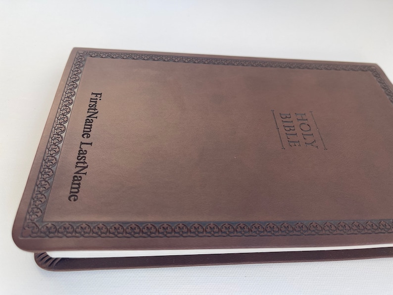 K&ouml;nnte beinhalten: Eine braune, ledergebundene Heilige Bibel mit einem dekorativen Rand und den Worten "HOLY BIBLE" auf dem vorderen Einband. Der Name "FirstName LastName" ist ebenfalls auf dem Einband gepr&auml;gt.