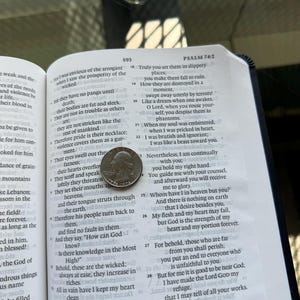 Pode incluir: Um livro aberto com texto, com uma moeda de vinte e cinco centavos na p&aacute;gina. O livro est&aacute; aberto no Salmo 74:2, com o n&uacute;mero 593 vis&iacute;vel. Os detalhes da moeda s&atilde;o parcialmente vis&iacute;veis.