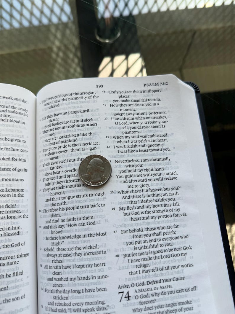 Pode incluir: Um livro aberto com texto, com uma moeda de vinte e cinco centavos na p&aacute;gina. O livro est&aacute; aberto no Salmo 74:2, com o n&uacute;mero 593 vis&iacute;vel. Os detalhes da moeda s&atilde;o parcialmente vis&iacute;veis.