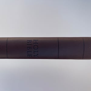 K&ouml;nnte beinhalten: Eine braune, ledergebundene Heilige Bibel mit den Worten "HOLY BIBLE" auf dem R&uuml;cken gepr&auml;gt. Der Text "NEW INTERNATIONAL VERSION" ist seitlich aufgedruckt.
