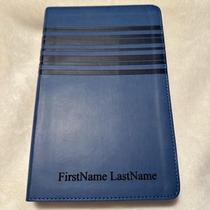 May include: A blue leather journal with black stripes and the name "FirstName LastName" embossed on the front.