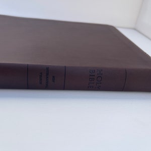 K&ouml;nnte beinhalten: Eine braune, ledergebundene Heilige Bibel mit dem Text "HOLY BIBLE" und "NEW INTERNATIONAL VERSION" auf dem R&uuml;cken.