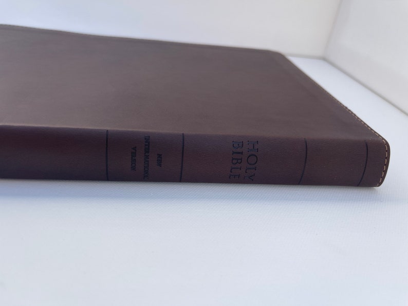 K&ouml;nnte beinhalten: Eine braune, ledergebundene Heilige Bibel mit dem Text "HOLY BIBLE" und "NEW INTERNATIONAL VERSION" auf dem R&uuml;cken.