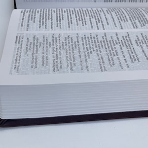 K&ouml;nnte beinhalten: Nahaufnahme eines wei&szlig;en Buches mit schwarzem R&uuml;cken. Das Buch ist auf einer Seite mit Text &uuml;ber die biblische Geschichte von Sisera aufgeschlagen. Der Text ist in Englisch.