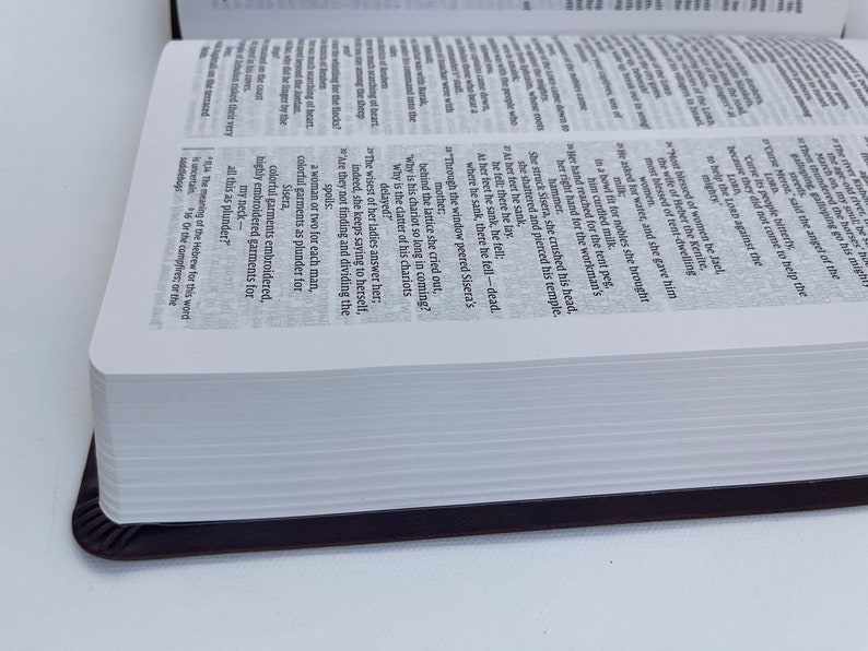 K&ouml;nnte beinhalten: Nahaufnahme eines wei&szlig;en Buches mit schwarzem R&uuml;cken. Das Buch ist auf einer Seite mit Text &uuml;ber die biblische Geschichte von Sisera aufgeschlagen. Der Text ist in Englisch.