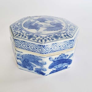 Könnte beinhalten: Achteckige Porzellandose mit blau-weißem Blumen- und Vogelmuster. Der Deckel zeigt drei Vögel im Flug, umgeben von einem floralen Rand. Die Seiten der Dose zeigen detaillierte Blumen- und Vogelmotive. Die Dose ist ein dekorativer Aufbewahrungsgegenstand.