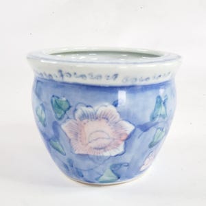 May include: A small, round, blue ceramic planter with a floral design. The planter features a light blue background with a pink and white flower and green leaves. The rim has a decorative pattern.