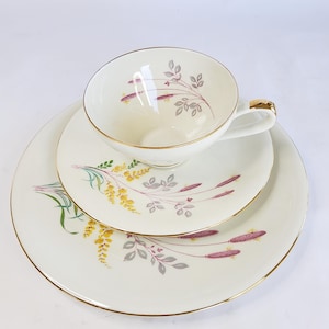 Può includere: Servizio da tè vintage in porcellana bianca con bordo dorato. Il set comprende una tazza, un piattino e un piatto, decorati con motivi floreali gialli, viola e grigi. Perfetto per il tè.