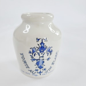 May include: A white ceramic jar with a rounded body and a narrow neck. It features a blue floral design and text that reads "Forte au Vin Blanc". The jar weighs 140g.