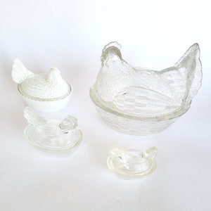 May include: Set of four clear glass chicken-shaped butter dishes. The largest dish features a chicken sitting in a nest. The other three dishes are smaller and feature a chicken without a nest.
