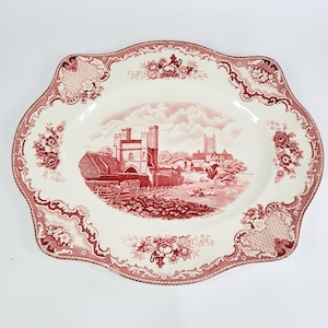 Może przedstawiać: Biała owalna półmisek z czerwono-białym wzorem kwiatowym. W centrum półmiska znajduje się czerwono-biała ilustracja zamku i otaczających go budynków.