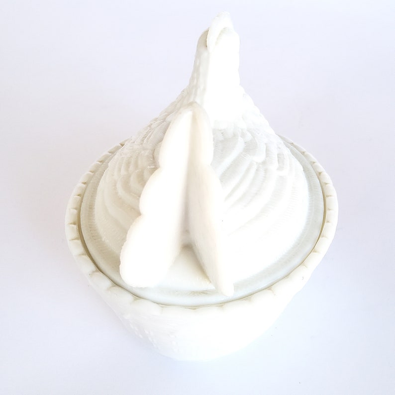 May include: White ceramic chicken-shaped trinket box with a detailed design. The lid is shaped like a chicken's head and has a raised comb.