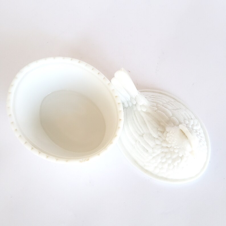 May include: White ceramic chicken-shaped dish with a lid. The lid is detailed with a raised design of feathers. The dish is empty.