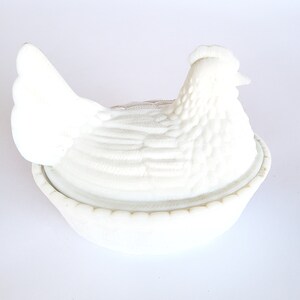 May include: White ceramic chicken shaped butter dish with a lid. The chicken is sitting on a nest.