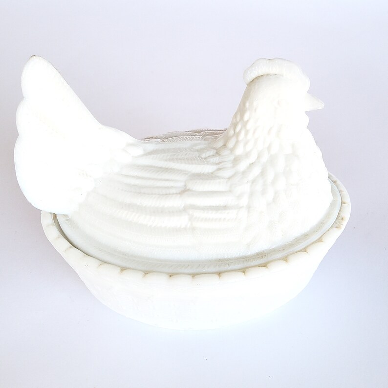 May include: White ceramic chicken shaped butter dish with a lid. The chicken is sitting on a nest.