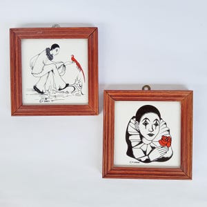 Könnte beinhalten: Zwei gerahmte Kunstwerke mit Pierrot-Figuren. Eines zeigt einen Pierrot mit einem roten Vogel, das andere einen Pierrot, der eine rote Rose hält. Beide sind Schwarz-Weiß-Illustrationen mit braunen Holzrahmen, ideal für die Wanddekoration.