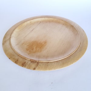 May include: A light-colored, oval wooden serving tray. The tray has a raised edge and a smooth, natural wood grain finish. The inner tray is slightly recessed, creating a layered effect. The overall design is simple and rustic.