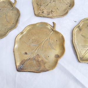 Puede incluir: Varios platos de latón con forma de hoja. Los platos tienen un diseño detallado de venas de hoja y un aspecto ligeramente deslustrado y antiguo. Los bordes de las hojas son suavemente curvados.