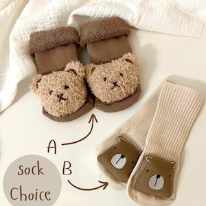 K&ouml;nnte beinhalten: Zwei Paar Babysocken mit B&auml;renk&ouml;pfen. Ein Paar ist braun mit flauschigen B&auml;renk&ouml;pfen und das andere Paar ist beige mit gestickten B&auml;renk&ouml;pfen. Der Text "Sockenwahl" ist auf dem Bild zu sehen.