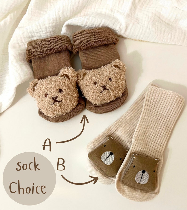 K&ouml;nnte beinhalten: Zwei Paar Babysocken mit B&auml;renk&ouml;pfen. Ein Paar ist braun mit flauschigen B&auml;renk&ouml;pfen und das andere Paar ist beige mit gestickten B&auml;renk&ouml;pfen. Der Text "Sockenwahl" ist auf dem Bild zu sehen.