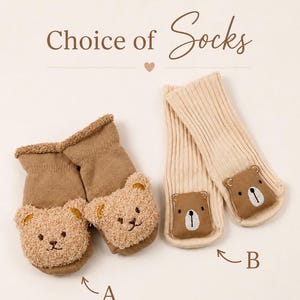 May include: Two pairs of socks labelled A and B with the text Choice of Socks. Pair A is brown with fuzzy bear faces. Pair B is cream-coloured with smooth brown bear faces. Each sock features a bear face appliqu&eacute; on the front of the foot area.