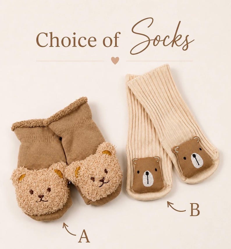 May include: Two pairs of socks labelled A and B with the text Choice of Socks. Pair A is brown with fuzzy bear faces. Pair B is cream-coloured with smooth brown bear faces. Each sock features a bear face appliqu&eacute; on the front of the foot area.