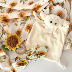 May include: A white plush lamb toy with a sunflower print headband, a crocheted sunflower rattle, and a white muslin swaddle blanket with a sunflower print.