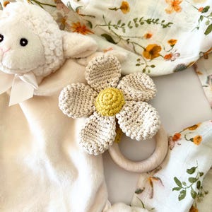 May include: A crocheted flower teether with a wooden ring, a plush white lamb toy, and a floral muslin swaddle blanket.