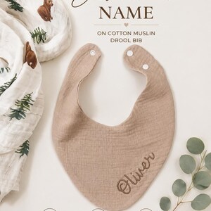 May include: A tan cotton muslin drool bib featuring the embroidered name Oliver in brown script. The bib has two white snap closures at the neck. Text on the image includes OPTION TO ADD Embroidered NAME ON COTTON MUSLIN DROOL BIB, 100% COTTON MUSLIN, SOFT & GENTLE ON BABY'S SKIN, and PERFECT FOR TEETHING & DROOL.