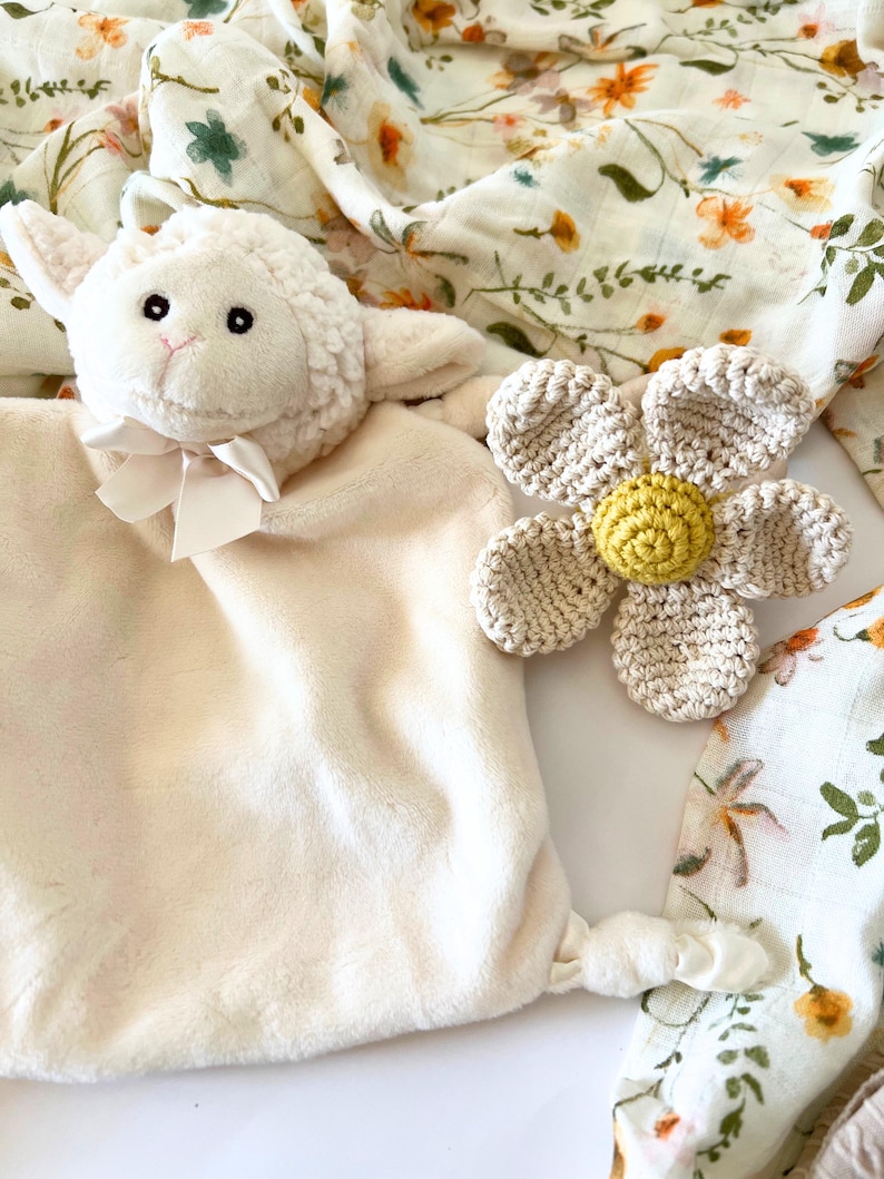 May include: A white plush lamb security blanket with a crocheted flower attached. The flower is beige with a yellow center. The blanket is made of soft, cuddly fabric and is perfect for babies and toddlers.