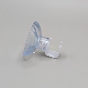 May include: A clear, transparent suction cup with a small, rectangular attachment. The suction cup is made of a flexible material and is designed to adhere to smooth surfaces. The attachment is rigid and appears to be made of plastic.