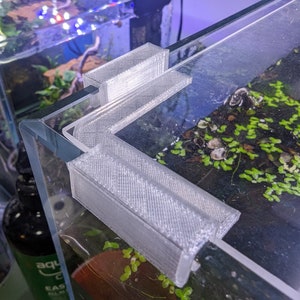 May include: A white 3D printed corner brace for an aquarium tank. The brace is designed to fit in the corner of the tank and help to support the glass.