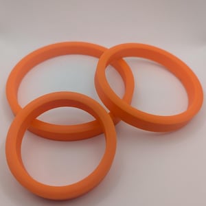 May include: Three orange silicone rings of different sizes. The rings are stacked on top of each other.