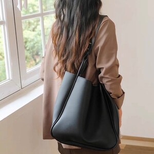 A women model is wearing a black leather shoulder bag for everyday use and laptop