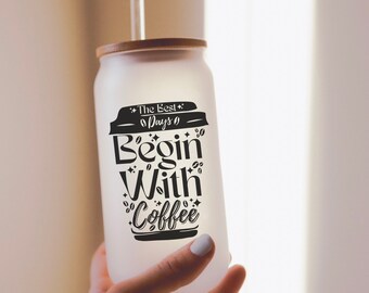 May include: A frosted glass tumbler with a bamboo lid and a clear straw. The glass features black text that reads The Best Days Begin With Coffee, decorated with small coffee bean and star icons printed on the front surface.