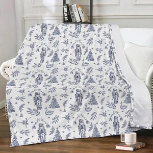 May include: White throw blanket with a blue and white pattern of nutcrackers, swans, and Christmas trees.