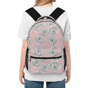 May include: A backpack with a pink background and a repeating pattern of black and white floral illustrations. The backpack has black shoulder straps and a black mesh side pocket. The person in the image is wearing a white t-shirt.