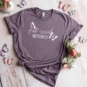 May include: A purple t-shirt with the text "Anti-social Butterfly" and two white butterfly silhouettes.