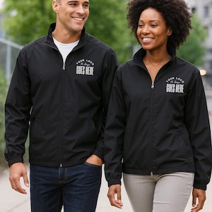 May include: Two people wearing black zip-up jackets. The jackets have a stand-up collar, side pockets, and the text "YOUR LOGO GOES HERE" printed on the chest. The person on the left is wearing a white t-shirt and blue jeans. The person on the right is wearing light-colored pants.