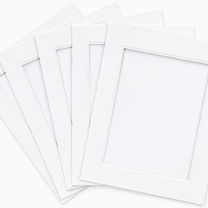 May include: A stack of white picture frame mats with rectangular openings. The mats are arranged in a fan shape, showcasing their clean, crisp edges and bright white color. Ideal for displaying photographs or artwork.
