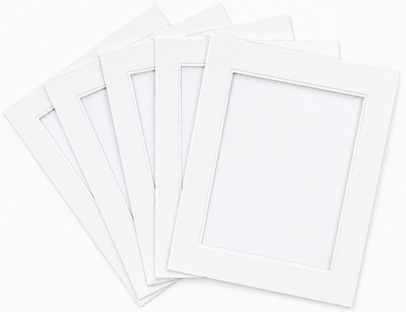 May include: A stack of white picture frame mats with rectangular openings. The mats are arranged in a fan shape, showcasing their clean, crisp edges and bright white color. Ideal for displaying photographs or artwork.