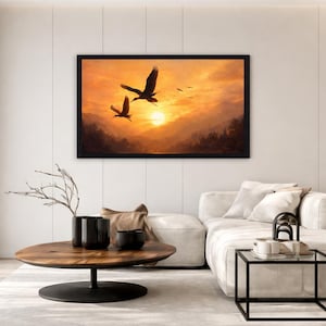 May include: A rectangular wall art piece in a black frame featuring a landscape painting of two birds flying over a mountain range during a golden sunset. The scene displays warm orange and yellow hues with silhouettes of trees and distant peaks.
