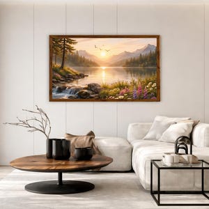 May include: A rectangular landscape painting in a dark wood frame depicting a serene mountain lake at sunset. The scene features a calm body of water reflecting the golden sun, surrounded by pine trees, rocky shores, and colorful wildflowers.