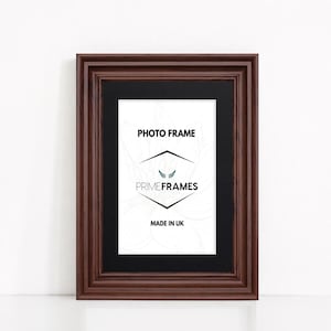 May include: A rectangular dark brown wooden photo frame featuring a black mat board. The centre insert displays the text PHOTO FRAME, the logo PRIME FRAMES with a small wing icon, and the text MADE IN UK, set against a faint white floral line drawing.